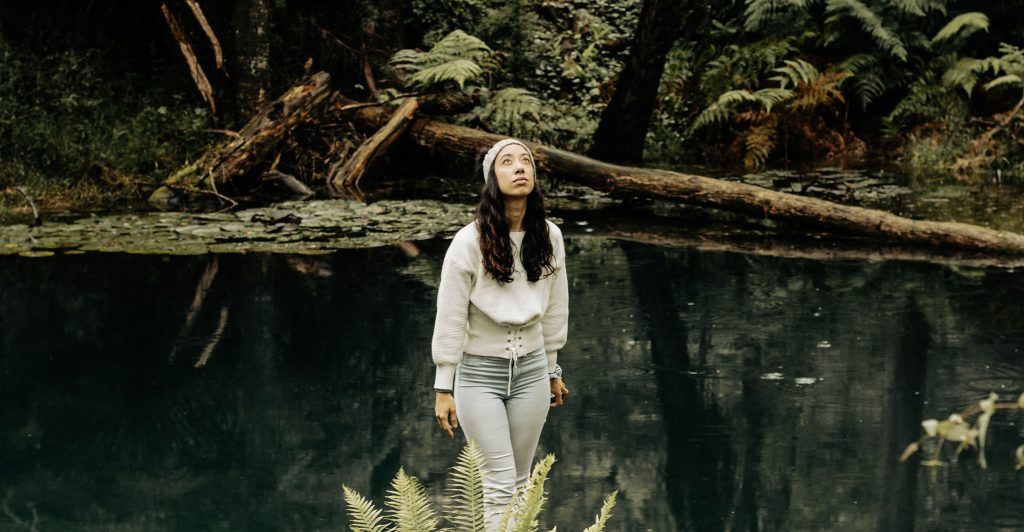 Image of woman in a rainforest looking up towards the sky.